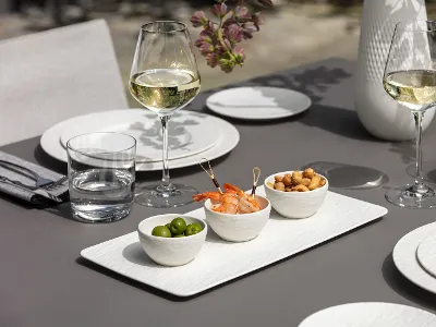 Elegant outdoor table setting with white Manufacture dinnerware, hors d'oeuvres and white wine.