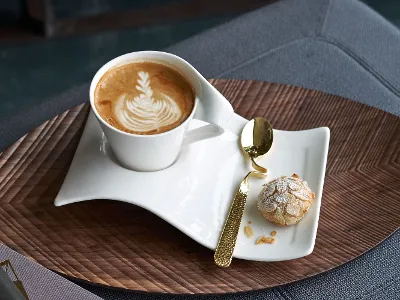 A NewWave cup with latte art and biscuits on a wooden table, together with a sophisticated NewWave spoon.