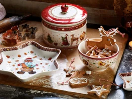 Ein festlich gedeckter Tisch mit Keramikgeschirr „Winter Bakery Delight“ von Villeroy & Boch sowie Keksen, einer dekorativen Blechdose, Ausstechformen und Backmehl, die auf einer Holzoberfläche verstreut sind.