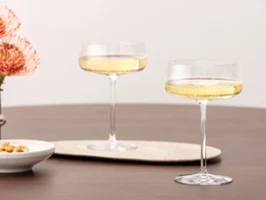 Deux verres Afina remplis de vin pétillant sur une table en bois, à côté de fleurs et d'un petit bol.