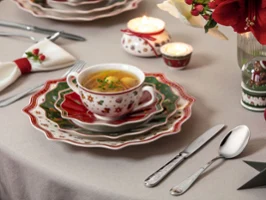A festively set table with a cup of soup, layered festive plates, cutlery, candles, and holiday decorations.