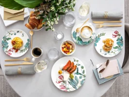 Table set for a meal with flower plates, food, drinks, napkins and a small bouquet of flowers as table decoration.