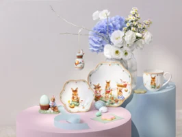 Assorted Annual Easter edition 2026 dishware with bunny designs displayed with flowers and decorative eggs on pastel stands.