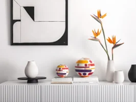 A minimalist sideboard showcases the modern La Boule Miami, vases, bird of paradise flowers, and stacked books under abstract wall art.