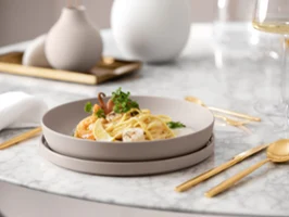 A plate of pasta with prawns, garnished with herbs, on an elegant dining table with gold cutlery and a glass of white wine.