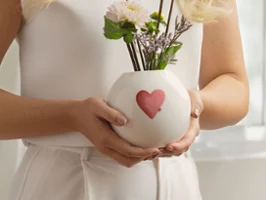 Woman holding a round white with love vase with a red-pink heart and white flowers.