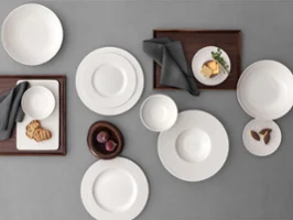 A formal table setting with a Manufacture plates A formal table setting with a white bowls and plates on a grey table and food on it.