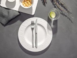 A plate with a crossed fork and a knife on it, a glass of water with lime next to it and two bowls of snacks on a table.