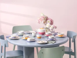 A pastel blue round table with a floral tea set consisting of colorful teacups, saucers, plates, and a teapot from the Fleur collection.