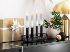 Ein Black Xmas Adventskalender mit vier Kerzen und ein goldverpacktes Geschenk mit einer weißen Schleife.