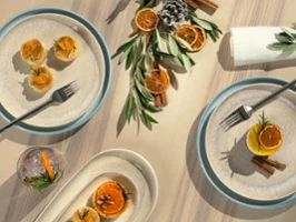 Scandinavian Christmas table setting with Perlemor dinnerware Top-down view of a light wooden table styled in a Scandinavian Christmas look with Villeroy & Boch's Perlemor porcelain plates, small pastries decorated with candied orange slices, cinnamon sticks, olive branches, and elegant cutlery.