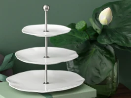Dreistöckiges weißes Pura Etagere mit Metallgriff, daneben eine große grüne Lotuspflanze und eine geschlossene Geschenkbox.
