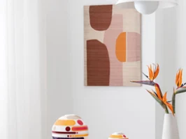 Modernes Interieur mit La Boule und La Petite Boule, einer weißen Vase Manufacture Collier blanc mit orangefarbenen Blumen sowie abstrakter Wandkunst in sanften Tönen.