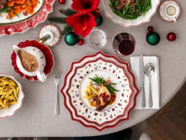 A festively laid table with decorated plates, wine glasses and a centrepiece of red flowers and ornaments.