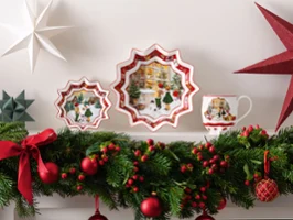 Eine weihnachtlich gestaltete Präsentation besteht aus zwei "Toy´s Fantasy" Tellern von Villeroy & Boch, einer "Toy´s Fantasy" Tasse, Papiersternen und einer üppigen Girlande mit roten Bändern, Ornamenten und Beeren auf einem weißen Kaminsims.