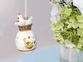 Ornement en céramique Annual Easter Edition 2026 avec un motif de poule suspendu près d’un bouquet de fleurs vertes et blanches dans un vase.