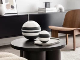 Ein moderner Wohnraum mit einer schwarz-weißen La Boule von Villeroy & Boch neben der schwarz-weißen La petite Boule auf einem dunklen runden Tisch. 