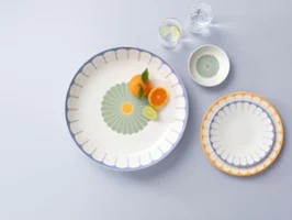 A large plate with orange slices and a mint leaf, next to two smaller plates and two glasses of water, on a light grey surface. A large plate with orange slices and a mint leaf, next to two smaller plates and two glasses of water, on a light grey surface.