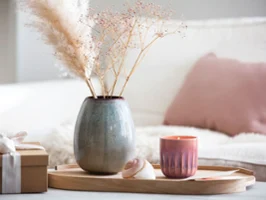 Holztablett auf dem eine Lave Vase und eine Perlemor Kerze mit getrockneten Blumen stehen, neben einem verpackten Geschenk.