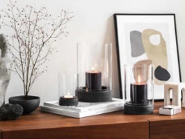 Eine moderne Wohneinrichtung mit einem hölzernen Sideboard und Trockenblume mit drei Manufacture Windlichtern. 