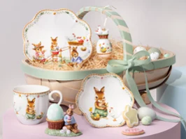 Un panier décoratif Annual Easter Edition 2026 avec des assiettes à thème lapin, une tasse, une figurine, des biscuits, des œufs et un ruban vert.