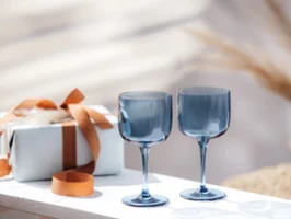 Deux verres à vin Like Glass de Villeroy & Boch en bleu sur une table blanche à côté d’un cadeau emballé avec un ruban marron.
