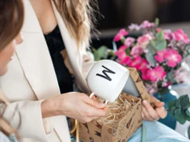 A woman holding a Letters cup with an "M". Another woman is sitting next to her with a smartphone.