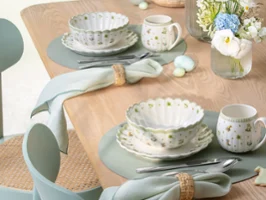 Une table en bois dressée avec des bols Easter Delight Une table en bois dressée avec des bols, des tasses, des assiettes, des serviettes et un petit arrangement floral Easter Delight.