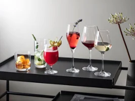Différentes boissons dans des verres La Divina, présentées sur un plateau noir moderne, garnies d’herbes et de fruits.