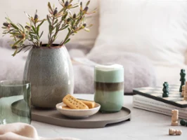  Un verre Like Sage avec du café, un échiquier, des biscuits et un vase Lave avec de l’herbe de la pampa sur un plateau de table.