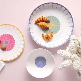 Trois assiettes Fleur de Villeroy & Boch Trois assiettes Fleur de Villeroy & Boch avec des croissants et des macarons, à côté de fleurs blanches sur un fond rose clair.