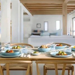 Une table à manger en bois pour quatre personnes avec des assiettes bleues nacrées Aqua Tell Une table à manger en bois pour quatre personnes avec des assiettes bleues nacrées Aqua dans un salon lumineux et moderne.