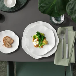 Une assiette Pura avec des légumes et une assiette d'accompagnement sur une table grise Une assiette Pura avec des légumes et un œuf, une assiette d'accompagnement avec du pain et des couverts sur une serviette posée sur une table grise.