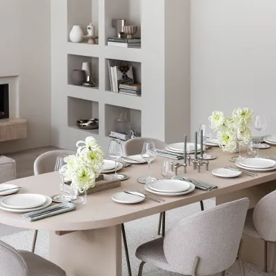 Vue latérale d’une table dressée avec de la vaisselle Afina et des couverts de table Piemont dans une pièce beige.