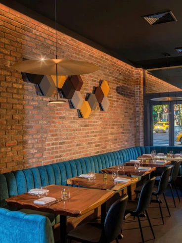 Inside of Arvine Restaurant Warm, modern restaurant interior with exposed brick, teal banquettes, wood tables, pendant lighting, geometric art, and a yellow taxi outside.