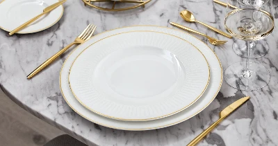 A white and gold dinnerware set from Château Septfontaines on a marble table.