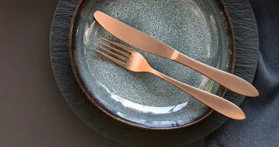 Une décoration de table élégante avec de la vaisselle moderne Manufacture et Lave ainsi que des couverts de table en cuivre de la collection Manufacture sur une nappe foncée.