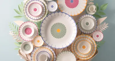 A collection of decorative plates from the Fleur collection A collection of decorative plates from the Fleur collection with colourful patterns arranged on a wall and surrounded by paper leaf decorations.
