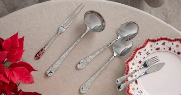 Toy's Delight cutlery On a beige table, next to an ornate plate and some red flowers, lies a set of serving cutlery and dining cutlery.