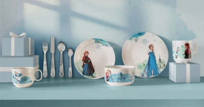 Stoviglie e utensili per bambini con personaggi di Frozen, esposti con scatole regalo blu su uno scaffale blu.