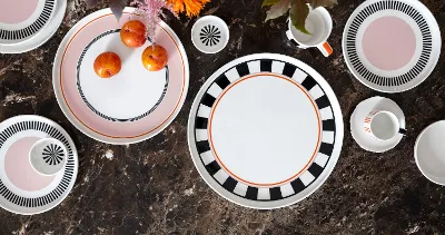 Service de table Memphis de Villeroy & Boch avec des assiettes décoratives, une tasse, des tasses et des prunes sur une surface en marbre brun décorée de fleurs brillantes.
