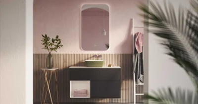 Une salle de bains moderne avec un plan de toilette noir, un lavabo Artis vert de Villeroy & Boch, une table d’appoint ronde avec une plante et un mur rose avec miroir. Un porte-serviettes avec des serviettes sur le côté droit et des feuilles de palmier partiellement visibles au premier plan.