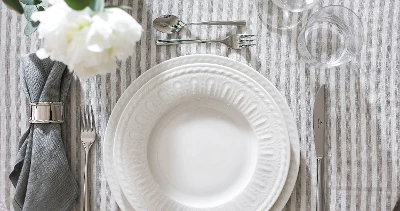 Elegant table decoration with white, embossed Cellini plate, flatware and folded gray napkin.