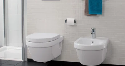 White Villeroy & Boch Architectura toilet and bidet Modern Architectura bathroom with a wall-mounted toilet, a bidet, a toilet roll holder and a towel holder with a blue-brown towel. The floor is covered with black tiles and there are small square white tiles on the wall.