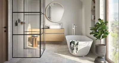 Une baignoire blanche Theano Curved Edition dans une salle de bains lumineuse avec une fenêtre allant jusqu’au sol.