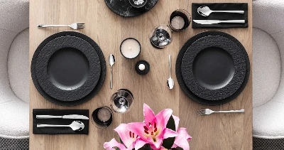 Modern table setting for two with black Manufacture dinnerware, Piemont flatware and pink lilies as the centerpiece.