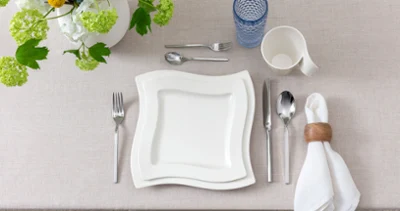 Modern top view of a single table setting featuring NewWave porcelain Vue du dessus d’un couvert individuel moderne et épuré avec assiettes et tasse en porcelaine NewWave, verre long drink Boston Blue et couverts assortis NewWave. Les tons neutres et l’esthétique minimaliste créent une impression contemporaine.