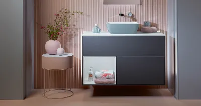 Mörkblått Finion-underskåp från Villeroy & Boch i ett rosa badrum med ett rosa soffbord.