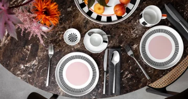 Colour explosion with Memphis by Villeroy & Boch A round marble table with two Memphis place settings, each with a plate, cutlery and a cup. A bowl of apples and a Memphis vase with flowers adorn the center.