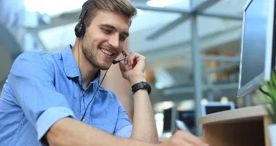 Smiling man with headset working on a computer in an office environment.